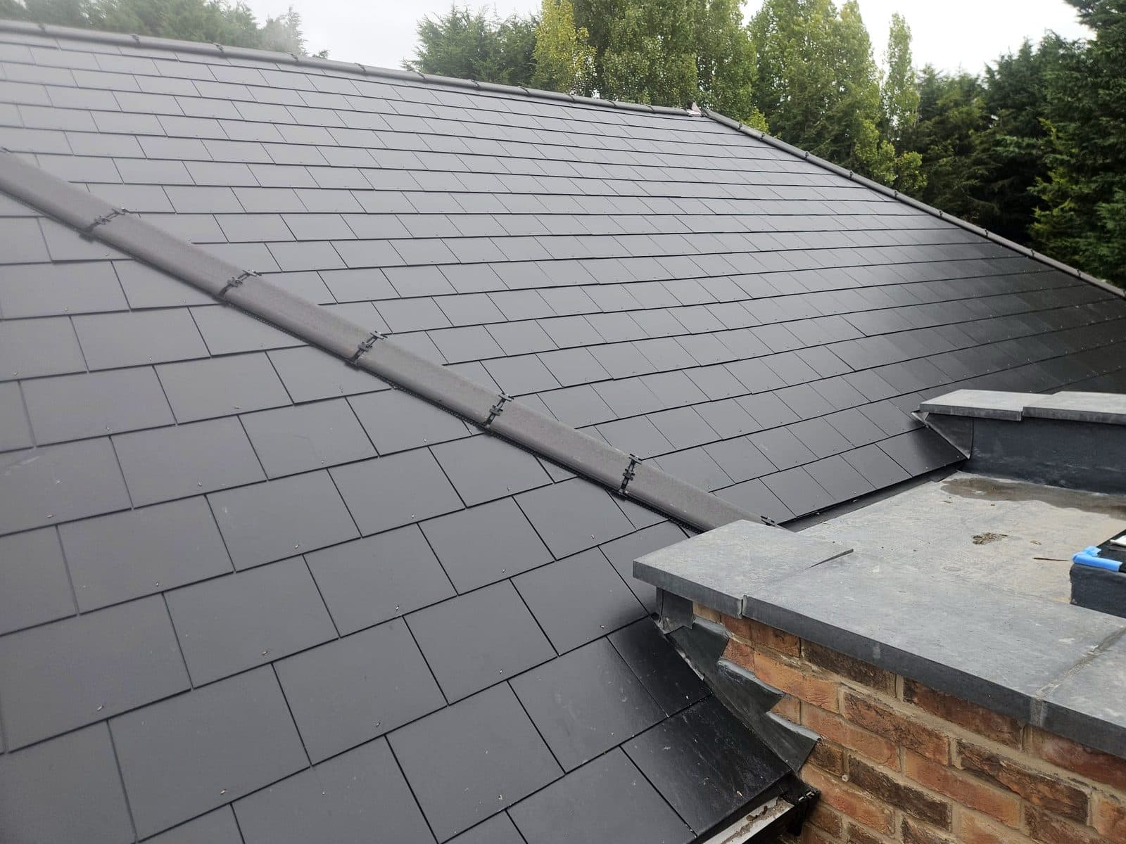 New slates meeting a parapet wall, with stepped lead flashing and new coping stones