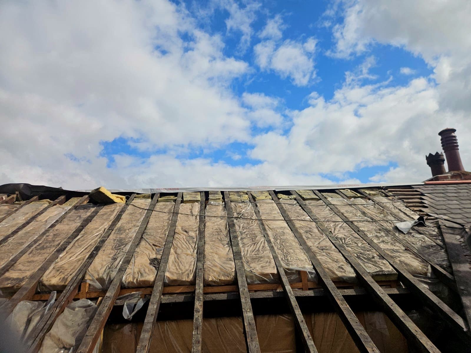A terrace roof stripped back to the old rafters, with the insulation showing between them