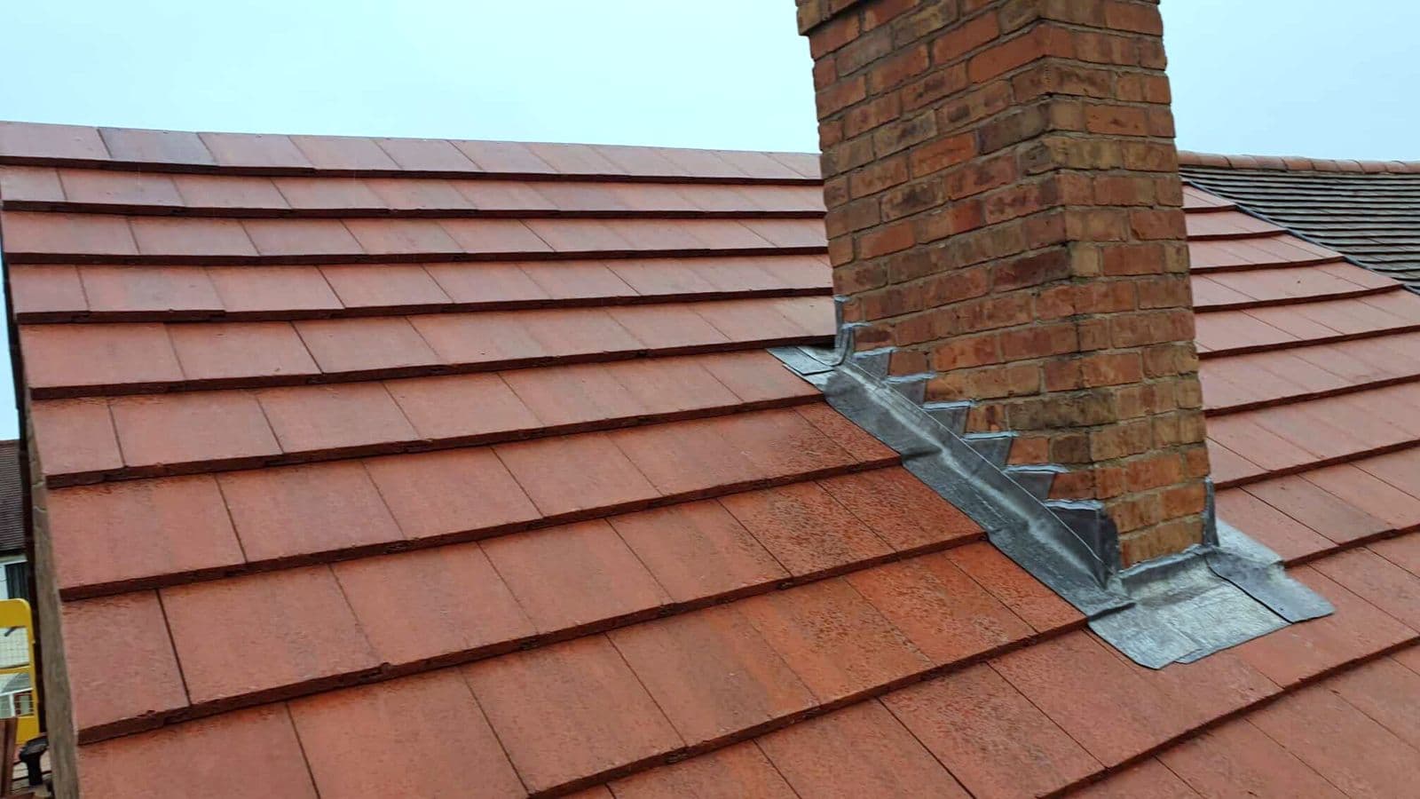 A repointed chimney with new leadwork on a clay tiled roof